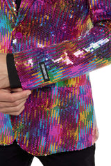 Someone adjusts the sleeve of a Rainbow Sequin Blazer by Suitmeister, showcasing a vibrant mix of pink, purple, blue, yellow, and green sequins. Beneath the blazer, theyre dressed in black.