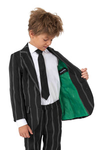 A young boy with tousled hair is wearing the Suitmeister Oversized Pinstripe Black suit, complete with a white shirt and black tie. He is holding open the jacket, revealing a bright green lining.