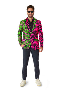 A man stands smiling, wearing sunglasses and a striking Party Animal Neon blazer by Suitmeister, featuring a green leopard print on one side and pink zebra stripes on the other. He's paired it with a black shirt, dark pants, and white sneakers.