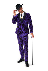 A man dressed in a "Pimp Faux Fur Purple" by Suitmeister, along with a black hat, is holding a black cane. He complements his look with a white shirt, a tie featuring a gold dollar sign, and black shoes against a plain white background.