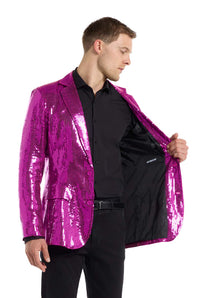 Dressed in a black shirt and pants, a man showcases the interior of his Sequins Blazer Pink from Suitmeister, which is fastened at the front. The blazer boasts a glossy, shimmering look with its vibrant magenta sequins. He stands against a white background.