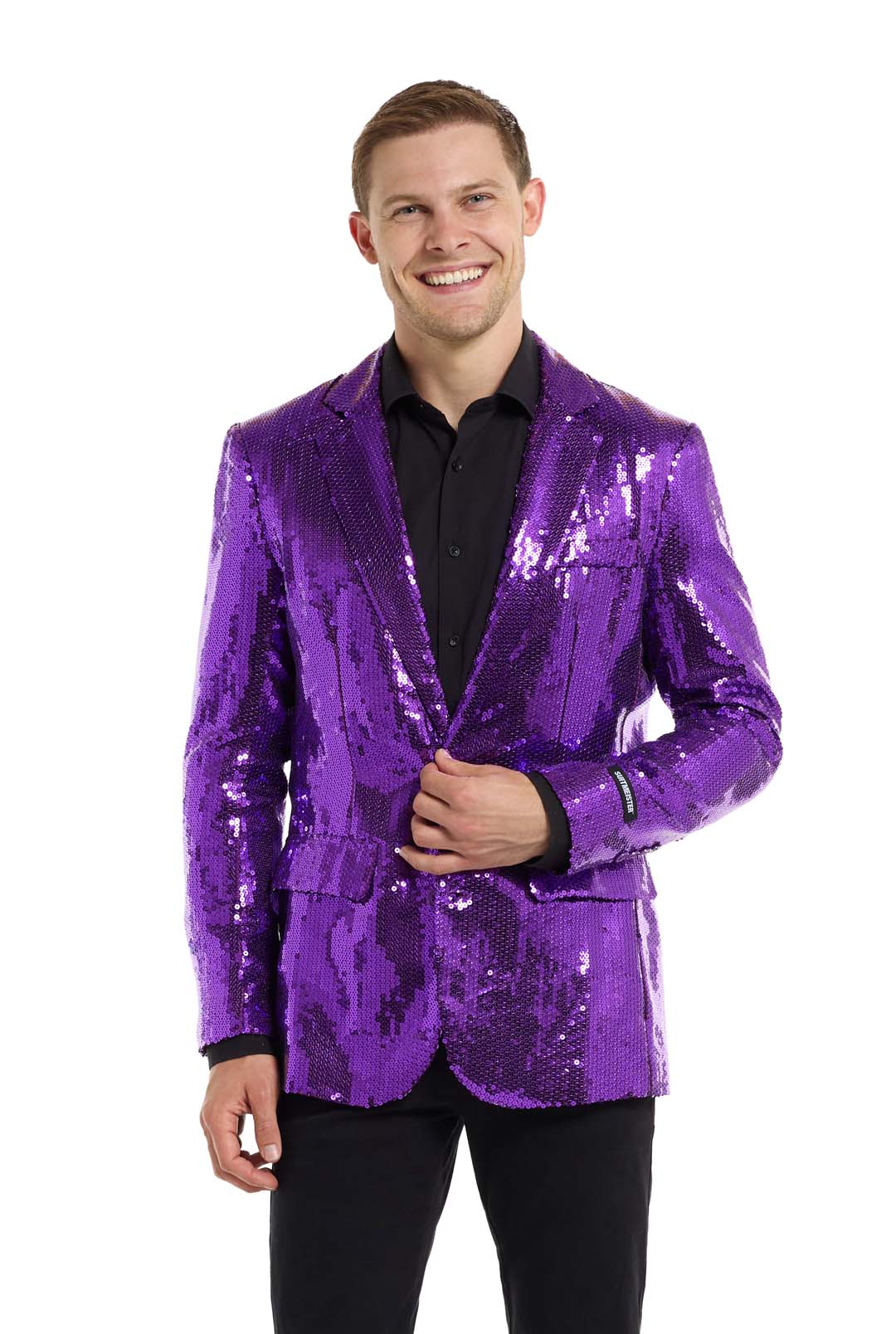 The individual is beaming while dressed in a shimmering purple "Suitmeister" Sequins Blazer over a black shirt and black pants, set against a simple white backdrop.