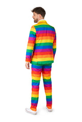 A person is standing with their back turned, dressed in a vibrant Suitmeister Rainbow suit featuring horizontal rainbow stripes. They have short hair and are paired with sleek white sneakers.