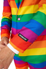 A person wearing a vibrant Rainbow suit from Suitmeister adjusts their sleeve against a plain white background.