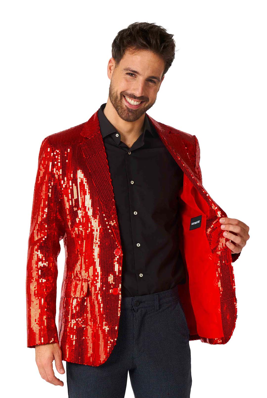 A man in a Suitmeister Sequins Blazer Red, paired with a black shirt and dark pants, smiles while holding one side of his open blazer.