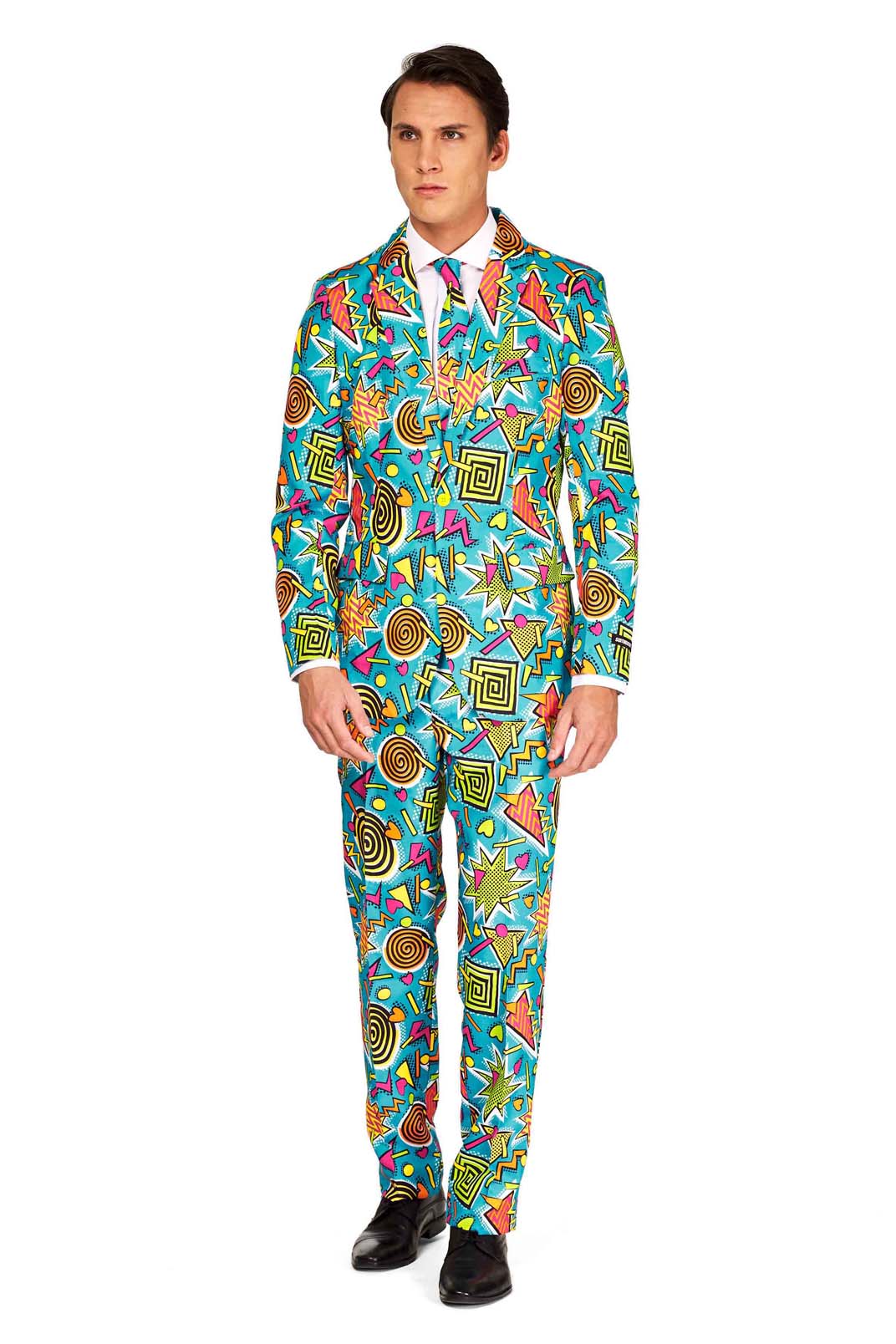 A man wearing the Retro Blue 90’s Icons - Carnival Suit by Suitmeister, featuring a colorful, abstract pattern with stars and geometric shapes. The suit is paired with a white shirt and red tie as he stands against a white background.