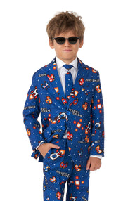 A young boy is dressed in the vibrant navy Retro Gamer suit by Suitmeister, featuring an 8-bit video game print with coins and the phrase "insert coin." He pairs it with a white shirt, a patterned tie, and sunglasses, his hands casually tucked in his pockets.