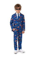 A young boy sporting the Retro Gamer Navy - Gamer suit by Suitmeister, complemented with sunglasses, is dressed in a blue suit that boasts colorful graphics and playful designs in red and orange hues. He pairs the suit with a white shirt, a blue tie, and stands confidently with his hands in his pockets wearing white sneakers.