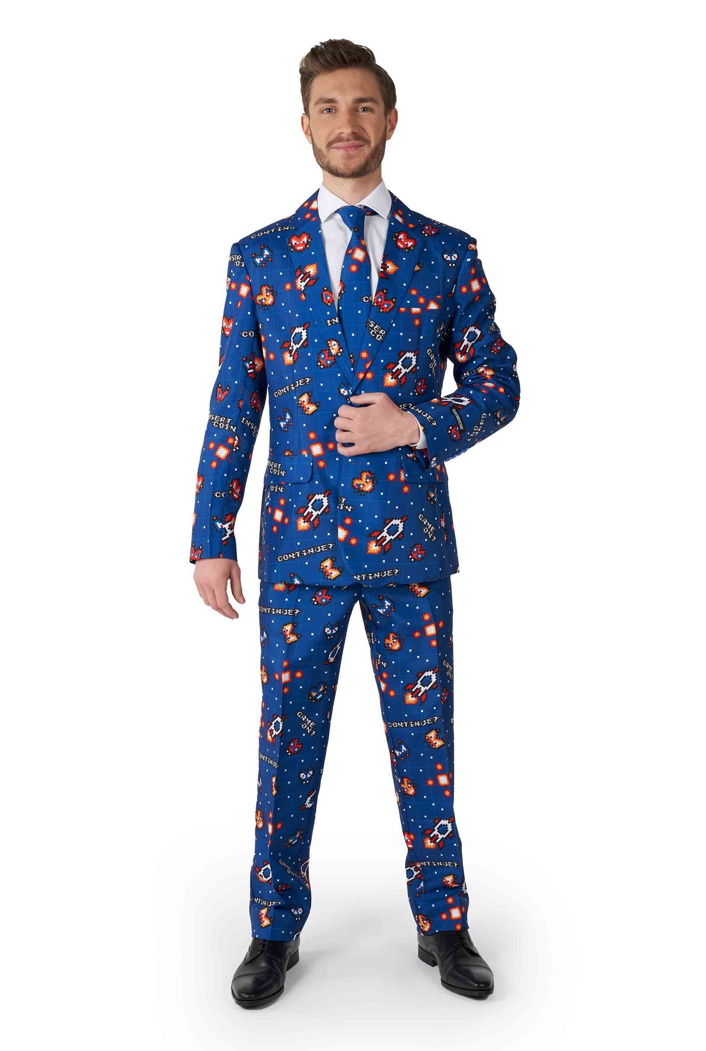 A man is dressed in the Retro Gamer Navy suit by Suitmeister, featuring colorful space-themed patterns with rockets and planets. He stands with one hand adjusting his jacket, paired with a white shirt, matching tie, and black shoes.