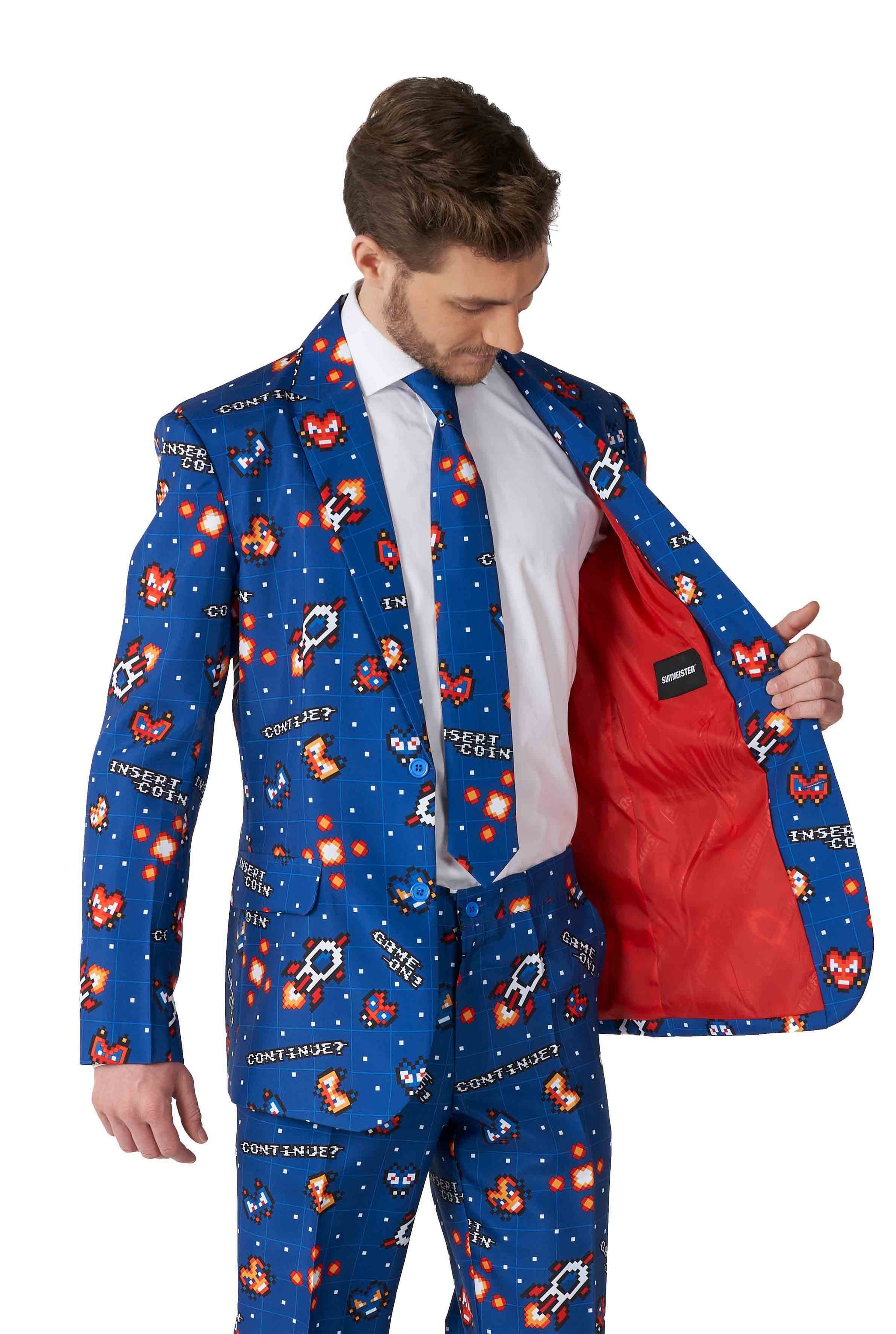 A man wearing the Retro Gamer Navy - Gamer suit by Suitmeister, featuring colorful pixel art designs and CONTEXT text. The inner lining of the suit jacket is red, and he holds one side open to reveal the interior.