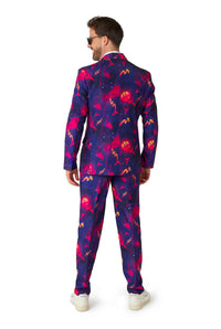 A man in sunglasses is wearing the Retro Neon Navy - Carnival suit by Suitmeister, showcasing a vibrant abstract pattern in shades of purple, pink, and red. He stands with his back to the camera, highlighting the matching jacket and pants.