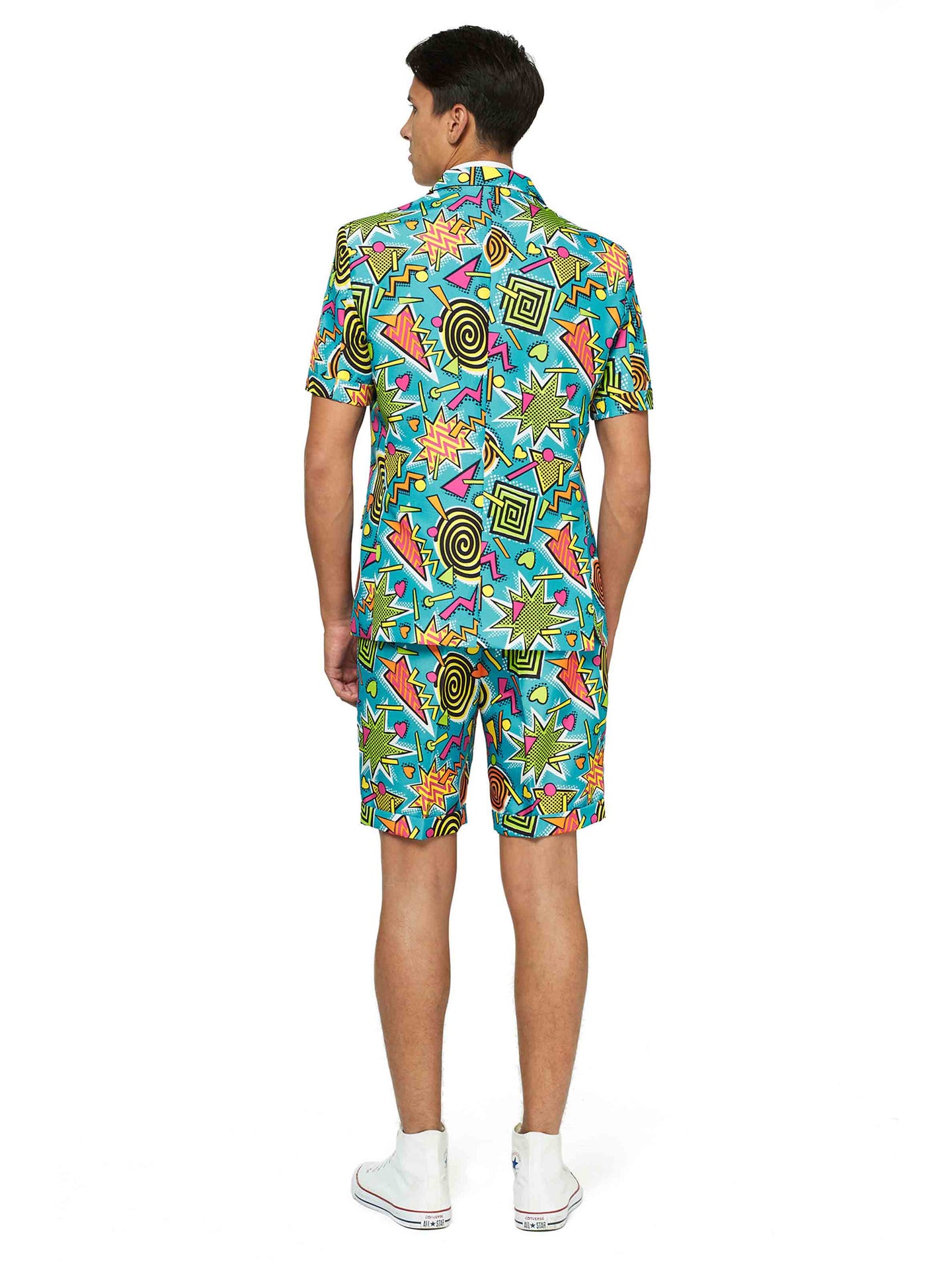 A man wearing the Suitmeister "Retro Blue 90’s Icons - Carnival suit," which includes a vibrant shirt and matching shorts adorned with geometric shapes in bright colors, stands facing away. He completes the look with white sneakers against a plain white background.