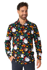 A person is smiling and wearing the Santa Elves Black - Christmas shirt by Suitmeister. The shirt features festive images of Santa Claus, gift boxes, and snowflakes on a dark background. They have short, dark hair and are standing against a white backdrop.