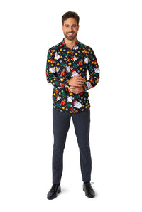 A man stands smiling in the Santa Elves Black - Christmas shirt by Suitmeister, showcasing festive holiday-themed designs. He has short, dark hair and a beard, paired with dark trousers and black shoes, set against a plain white background.