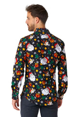 A man with short hair is facing away, wearing a vibrant Christmas-themed shirt from Suitmeister called the "Santa Elves Black." The shirt features Santa Claus, snowflakes, stars, and gift images on a predominantly black background with bright festive patterns.