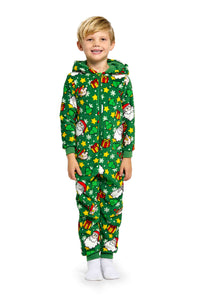 A smiling child is dressed in the Santa Elves Green - Christmas Onesie, designed by Suitmeister. The green holiday-themed onesie features prints of Santa Claus, snowflakes, and Christmas gifts and includes a hood. The child stands on a white background wearing white socks.