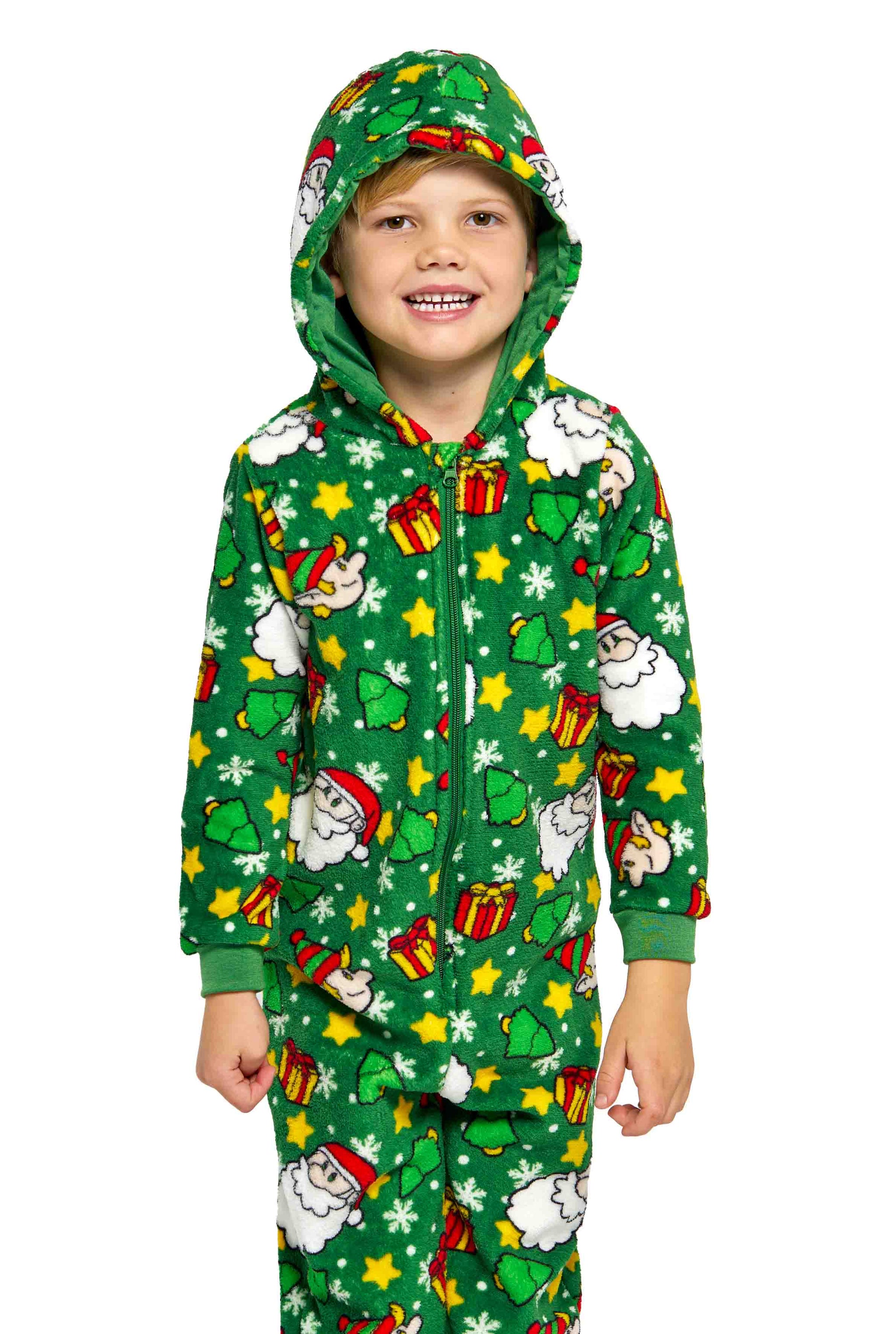 A young child is smiling while wearing the Suitmeister Santa Elves Green Christmas Onesie, featuring festive images of Santa, gifts, stars, and trees.