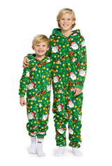 Two children smiling and dressed in matching Santa Elves Green - Christmas Onesies by Suitmeister, adorned with designs of Santa Claus and gifts. One child has their arm around the other, while they both wear white socks against a white background.