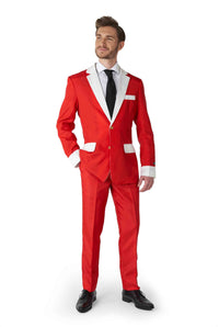 A man wearing the Suitmeister "Santa Faux Fur - Santa Christmas suit" stands confidently to the side. The bright red suit with white trim features a white shirt and black tie. His hand is in his pocket as he exudes confidence, with matching red pants and black shoes adding to the festive appearance.