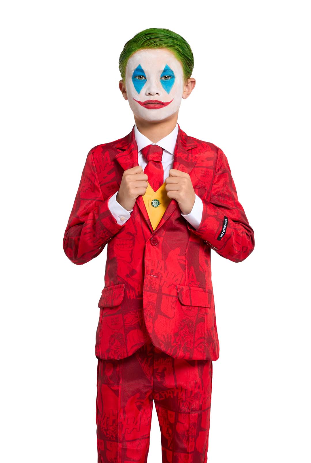 A child is dressed in the Scarlet Joker costume by Suitmeister, featuring a red suit adorned with comic designs, complemented by a yellow vest and a red tie. The face is painted white with blue triangles above and below the eyes, a bright red nose, and an exaggerated red smile, while the hair is strikingly colored green.