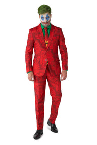 A person dons the Scarlet Joker™ ensemble from Suitmeister, featuring a vibrant red suit adorned with black designs, complemented by a green shirt and tie, and paired with classic black shoes. Their face is artistically painted in a clown-like manner using white, blue, and red makeup, complete with distinctive green hair.