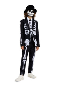 A person is dressed in the Skeleton Grunge Black suit by Suitmeister, which features a black jacket and pants with a white skeleton print. They are also wearing a black top hat, sunglasses, and white sneakers while standing against a white background.