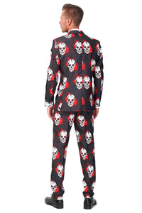 A person wearing the Suitmeister "Skulls Blood - Halloween suit" faces away, showcasing its black design with a pattern of white skulls and red splatters. The ensemble includes a matching jacket and pants. They have paired it with black shoes and have short hair, set against a plain white background.