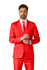 A man stands against a white background wearing a Solid Red suit from Suitmeister, paired with a white dress shirt and red tie. With a confident expression, he adjusts his cuffs.