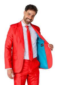 A man wearing a Solid Red suit by Suitmeister, along with a white shirt and red tie, smiles while holding open his jacket to reveal its light blue lining against a plain white background.