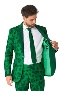 A man dressed in the Suitmeister St. Pats Green - St Patrick's Day suit, complete with a shamrock pattern, white shirt, and green tie. He is looking down as he opens one side of the suit jacket to reveal its inner lining.