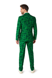 A man in the St. Pats Green suit by Suitmeister, adorned with dark green shamrocks, stands facing away. He has short brown hair and is wearing white shoes, creating a festive St. Patrick's Day appearance.