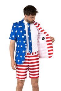 A man dressed in the USA Flag suit from Suitmeister, featuring a star-patterned blue jacket paired with striped red and white shorts and tie. The inside of the jacket showcases red and white stripes, mimicking the American flag design. He is inspecting the interior of his jacket.