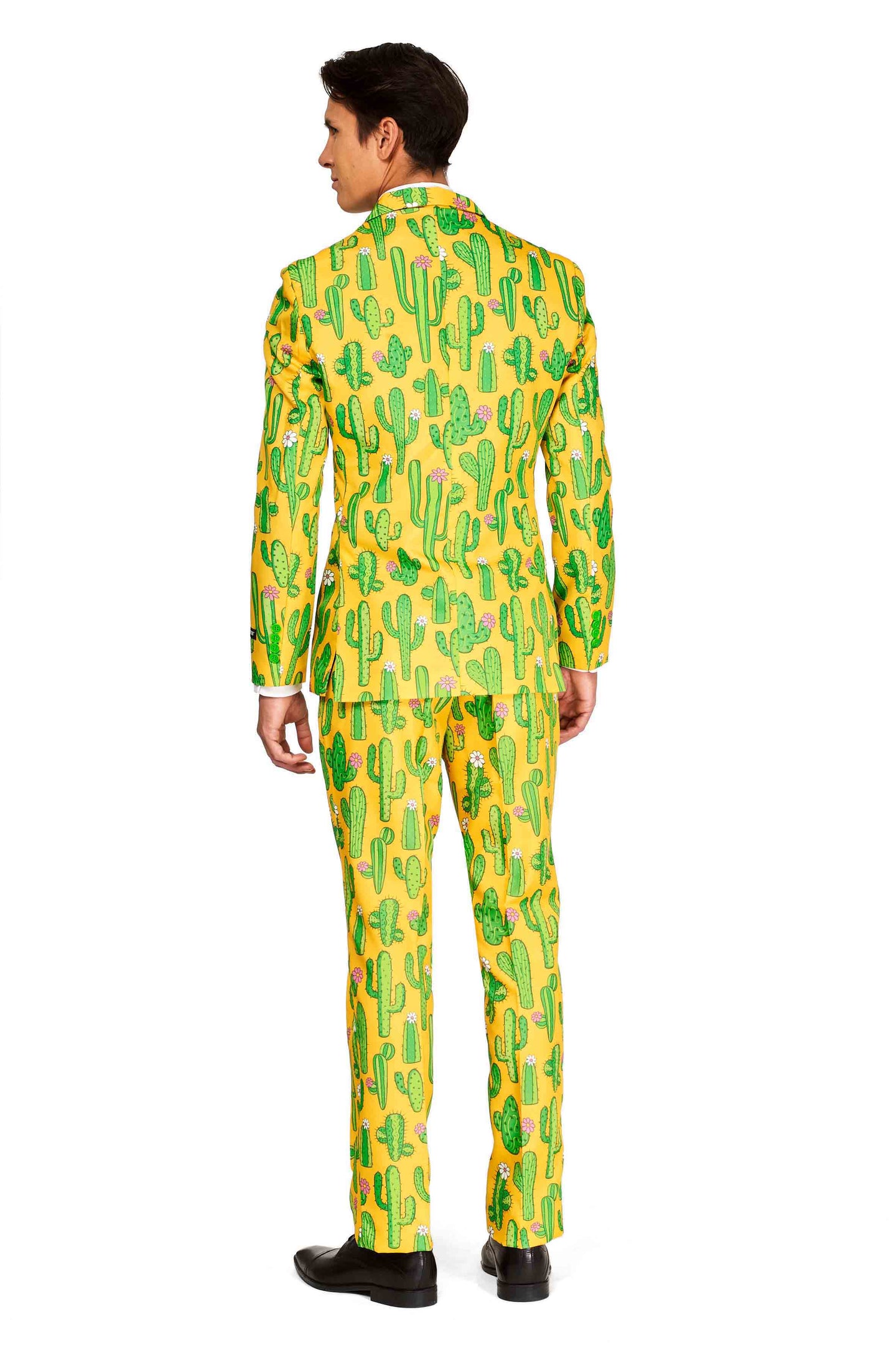 An individual stands wearing the "Sunny Yellow Cactus" Festival suit by Suitmeister, featuring a vibrant blazer and trousers adorned with a cactus pattern. They are facing away, showcasing the back of their colorful suit paired with black shoes. The white background accentuates the outfit's lively design.