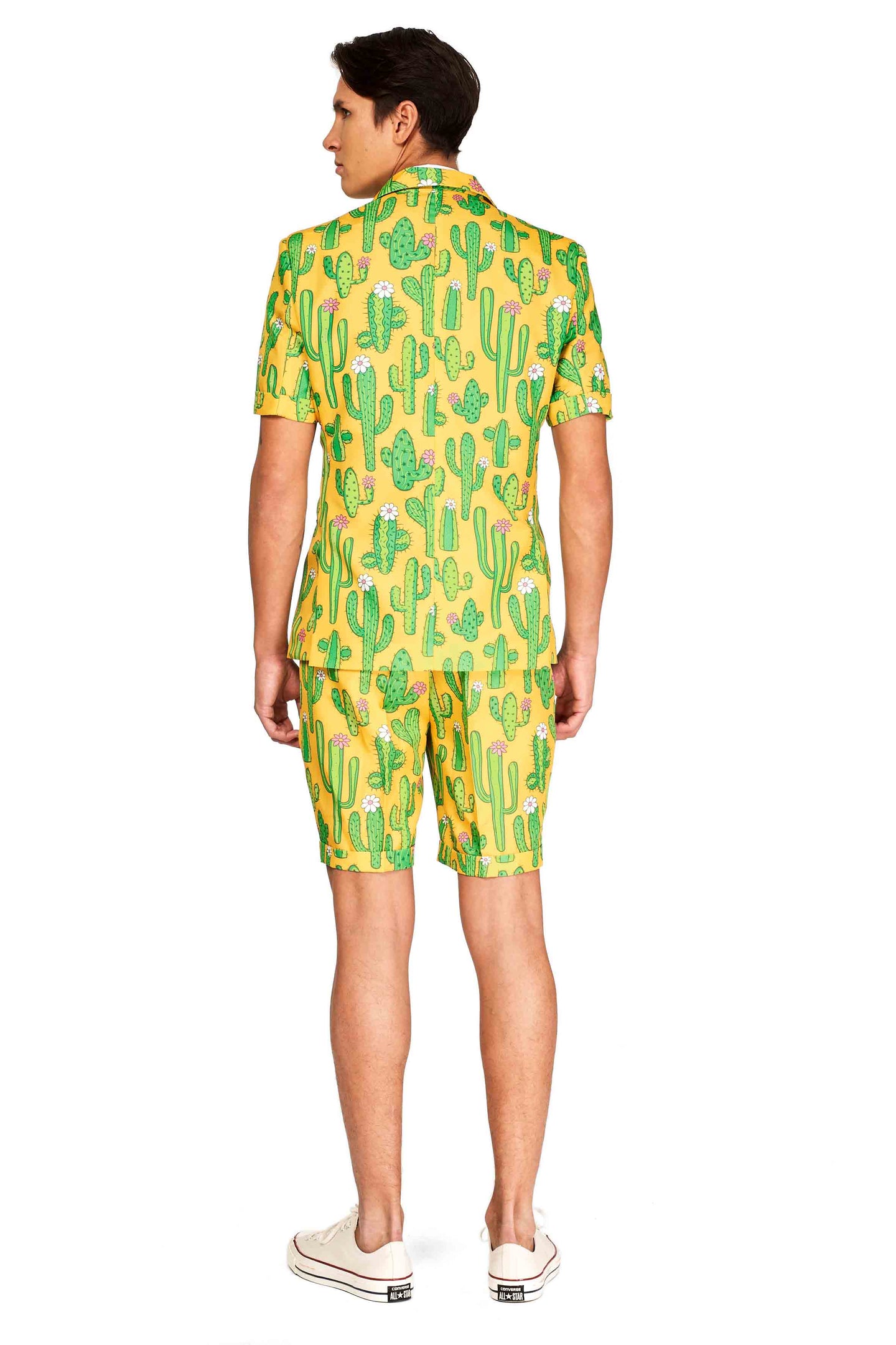 An individual is seen from behind wearing the "Sunny Yellow Cactus - Summer Suit" by Suitmeister, which features a short-sleeved jacket and matching shorts in a vibrant yellow with a playful green cactus design. They have paired it with white sneakers.