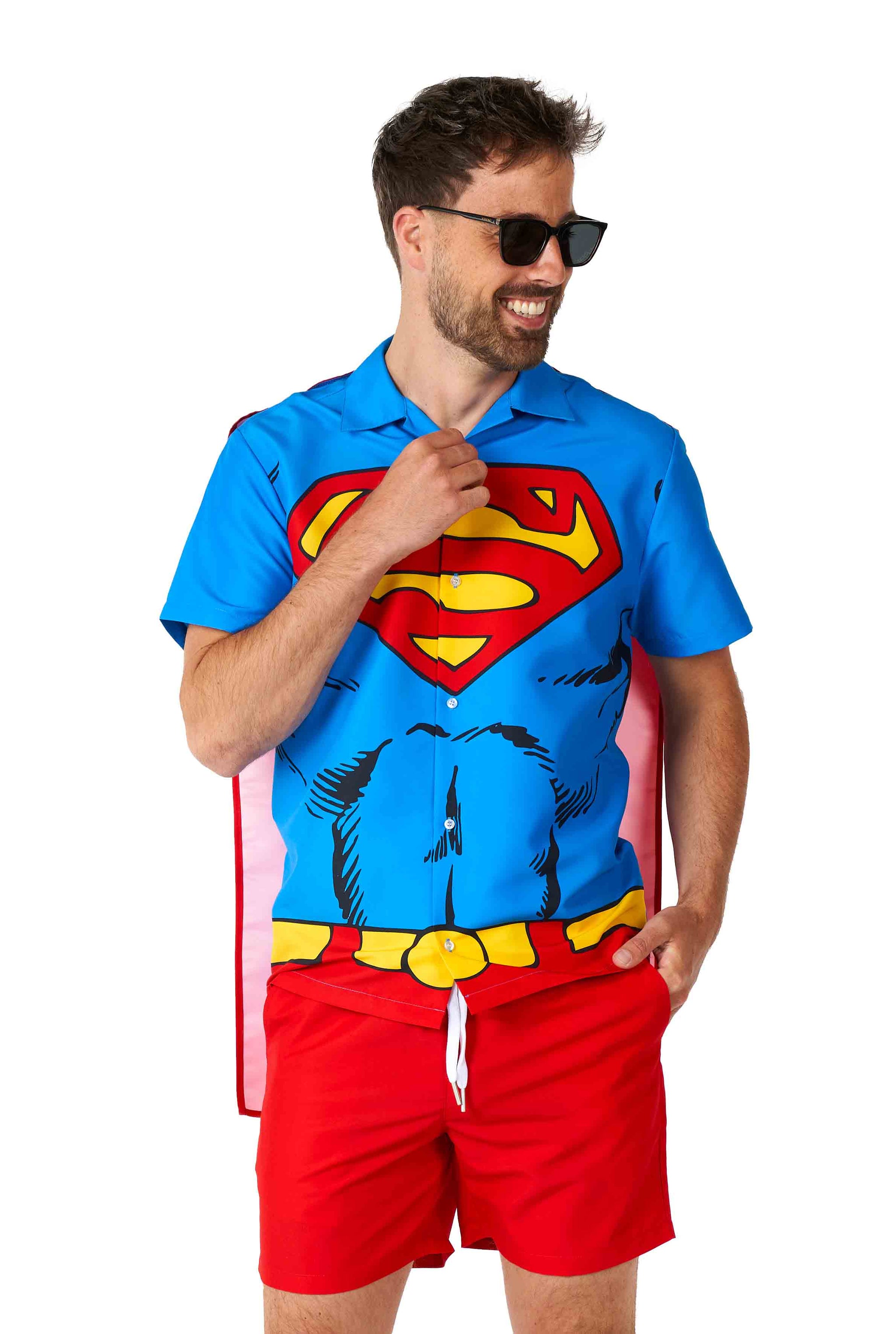 A man wearing sunglasses beams as he sports a Superman outfit from Suitmeister, featuring a blue shirt adorned with a red S emblem that mirrors a superhero costume. He completes the look with red shorts and an attached red cape, standing against a plain white background.