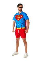 A man confidently poses in a Superman outfit by Suitmeister, featuring a blue superhero-themed shirt with a red and yellow logo, red shorts, white sneakers, black sunglasses, and a red cape.