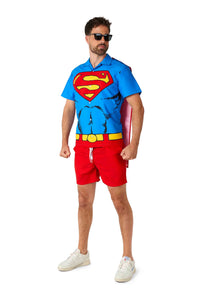 A man confidently poses in a Superman outfit by Suitmeister, featuring a blue superhero-themed shirt with a red and yellow logo, red shorts, white sneakers, black sunglasses, and a red cape.