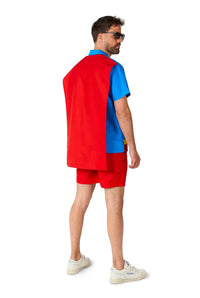 A man dressed in a Suitmeister Superman outfit, complete with a blue shirt, red cape, and red shorts, stands facing away on a plain white background. He wears white sneakers and sunglasses while looking to the side.