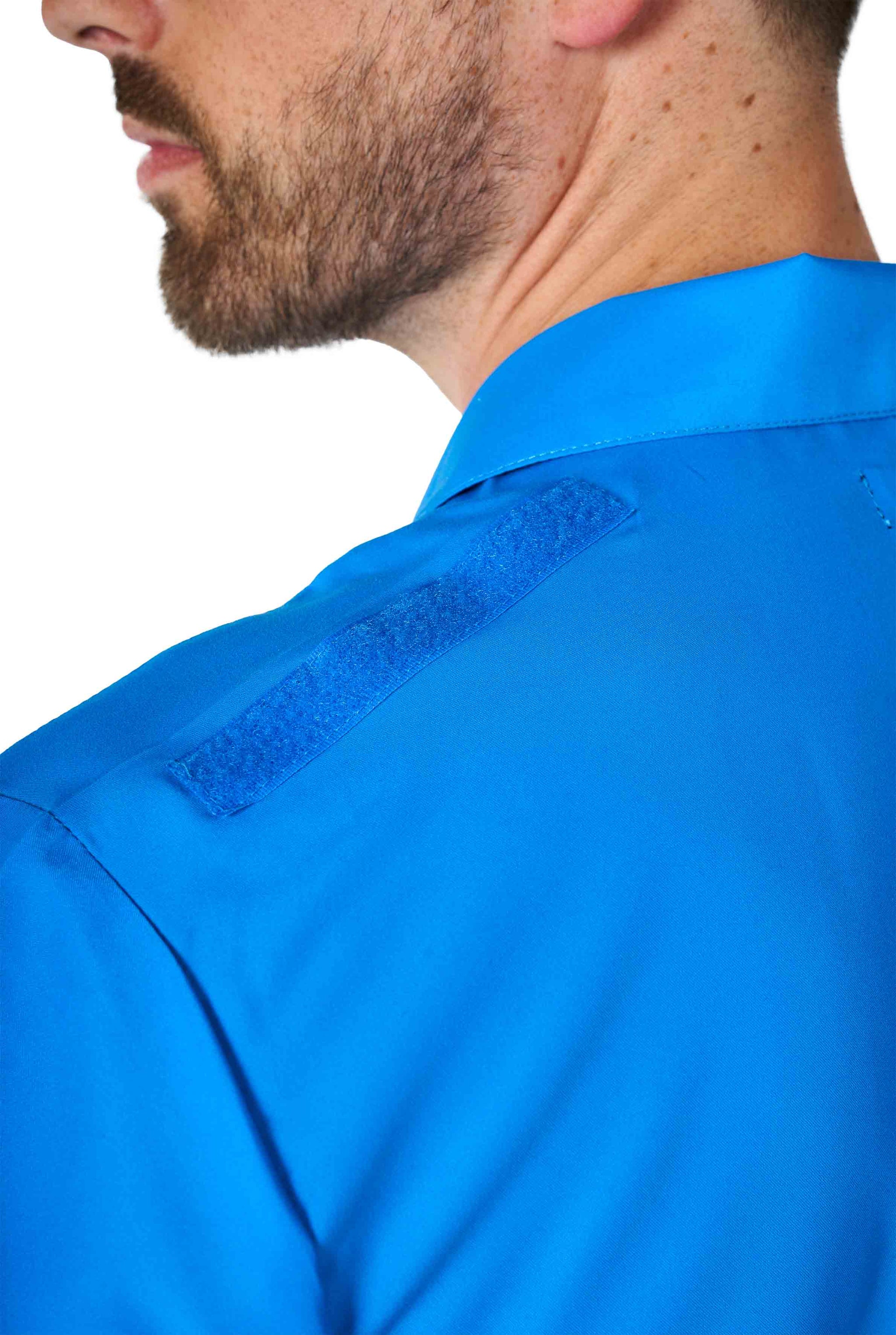 Close-up of an individual in a Superman outfit by Suitmeister, featuring a vibrant blue shirt with a Velcro patch on the shoulder. The person, who has a beard and is slightly turned away, highlights the detailed shoulder design.