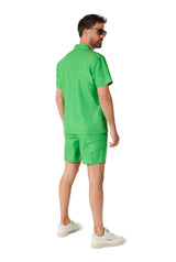 A man wearing sunglasses is standing and looking to the side, dressed in a Suitmeister TMNT outfit, consisting of a matching green short-sleeve shirt and shorts set, paired with white sneakers, against a white background.