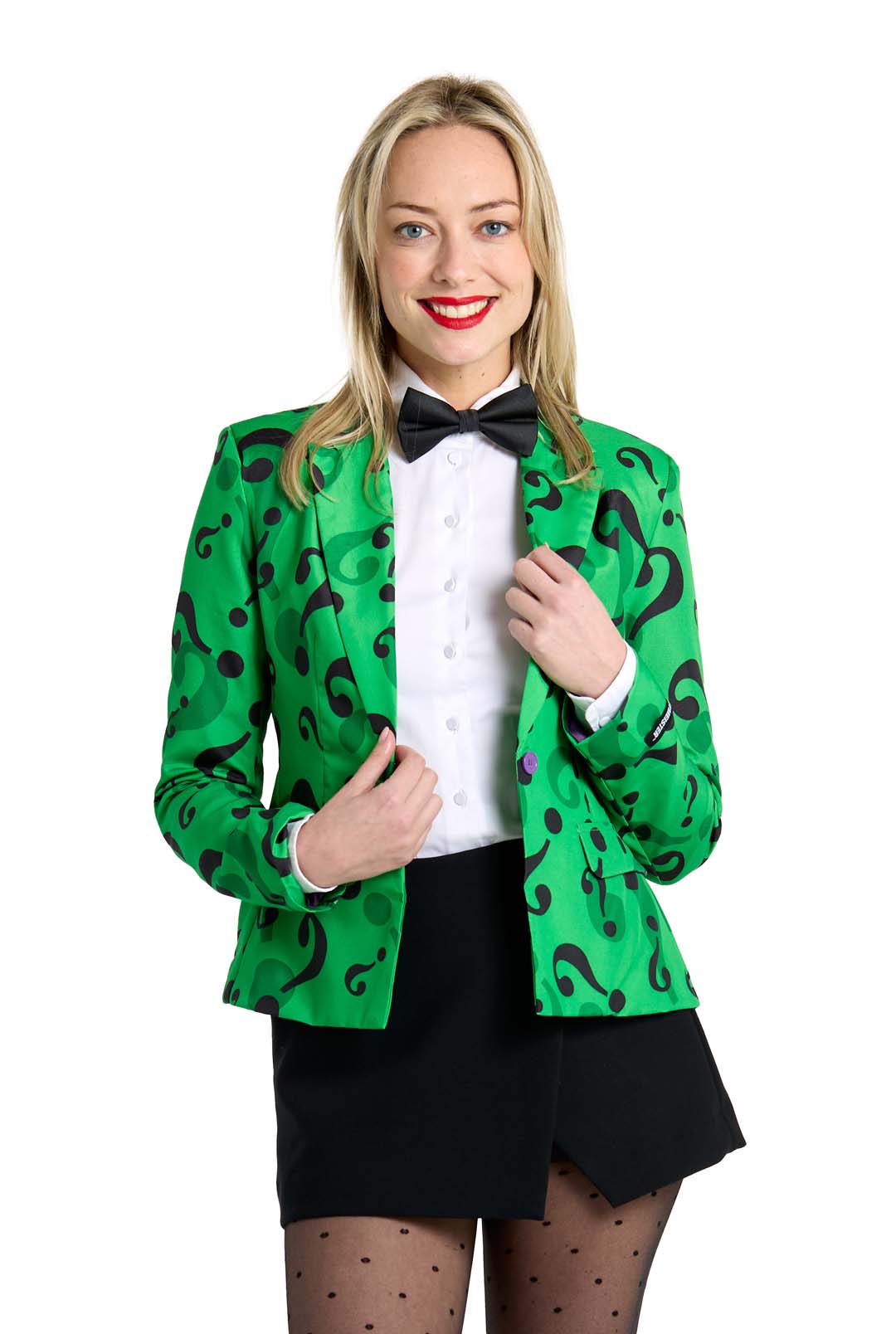 A person wearing The Riddler Jacket by Suitmeister, a green jacket with black question marks, is over a white shirt. They complement it with a black bow tie, a black skirt, and polka-dot stockings. Smiling, they hold the jacket with one hand.