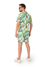 A man dressed in the Suitmeister Tropical Beers Blue - Festival suit, complete with matching shirt and shorts featuring a colorful tropical pattern, accessorized with sunglasses and white sneakers, stands facing away against a white background.