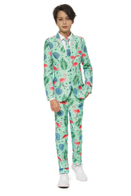 A young person stands confidently in a vibrant Suitmeister "Tropical" suit featuring pink flamingos and green tropical leaves on a light background. They pair it with white sneakers and a white shirt, one hand casually resting in their pocket, against a plain white backdrop.