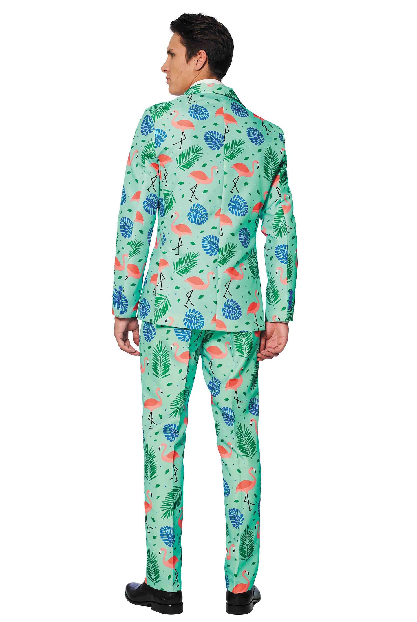 A person is standing with their hands relaxed by their sides, wearing Suitmeister's "Tropical" suit. The suit is colorful and features a green background with patterns of flamingos, leaves, and geometric designs. The individual has short dark hair and is facing away.