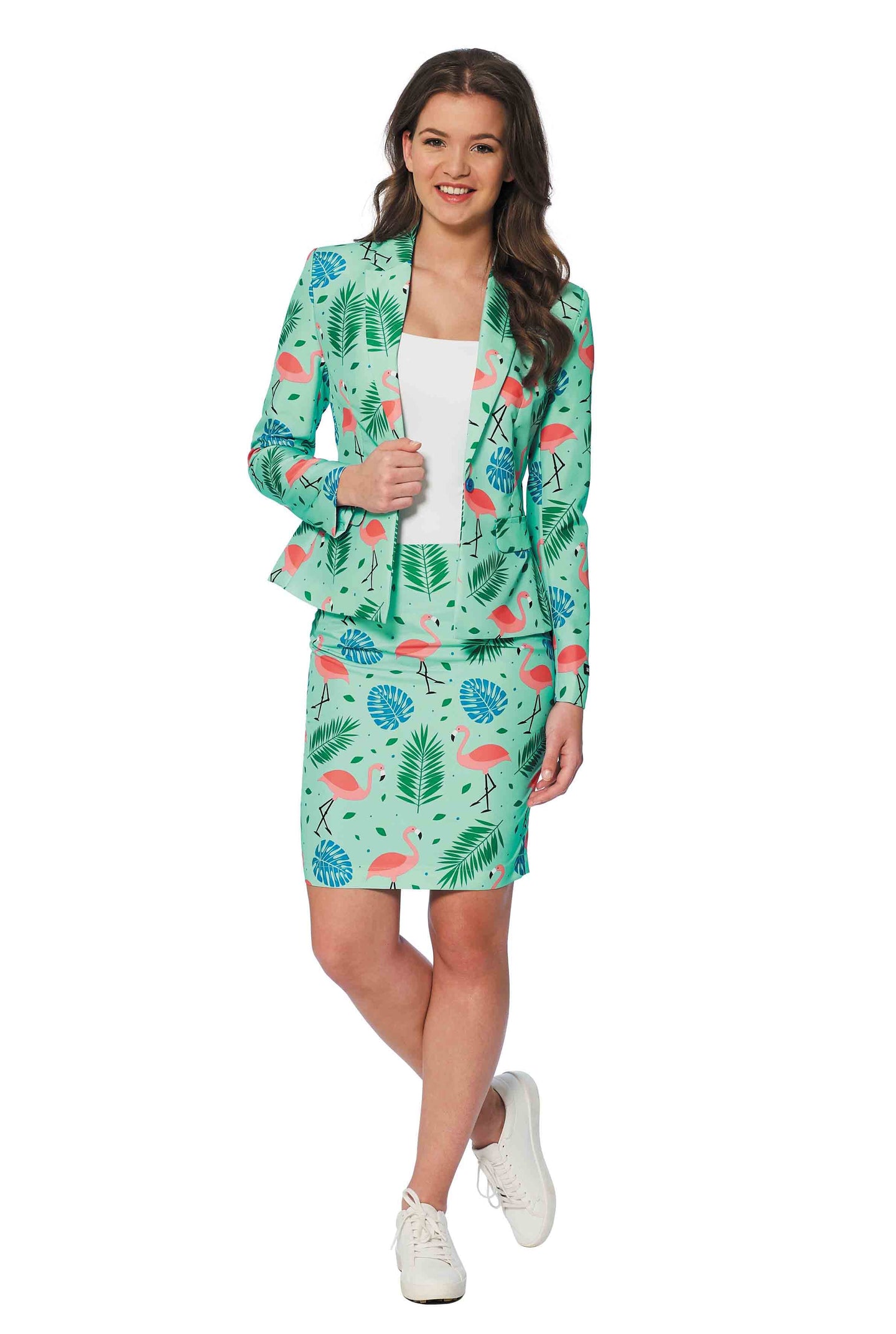 A woman is wearing Suitmeister's Tropical suit, adorned with a lively print of flamingos and palm leaves. She pairs it with a white top and white sneakers while smiling against a plain white backdrop.