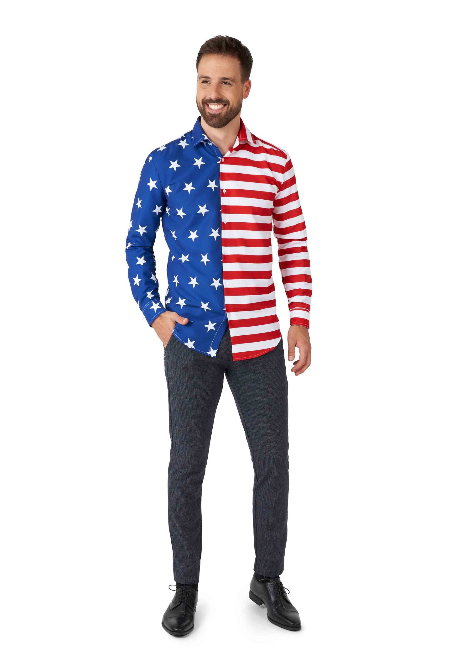 A man with a beard smiles, wearing the USA Flag shirt by Suitmeister, which features an American flag design with stars on the blue side and red and white stripes on the other. With one hand in his pocket, he pairs it with dark pants and black shoes while standing against a white background.