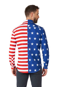 A man with short brown hair and a beard is wearing a Suitmeister USA Flag Shirt, featuring an American flag pattern. The right side showcases red and white stripes, while the left side displays blue with white stars. He is facing away from the camera.