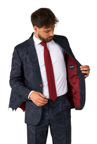 A man wearing the Suitmeister's Victorian Vampire Suit Black, which features a subtle decorative design, paired with a white shirt and red tie. He is opening the jacket to reveal its striking red lining against a white background.