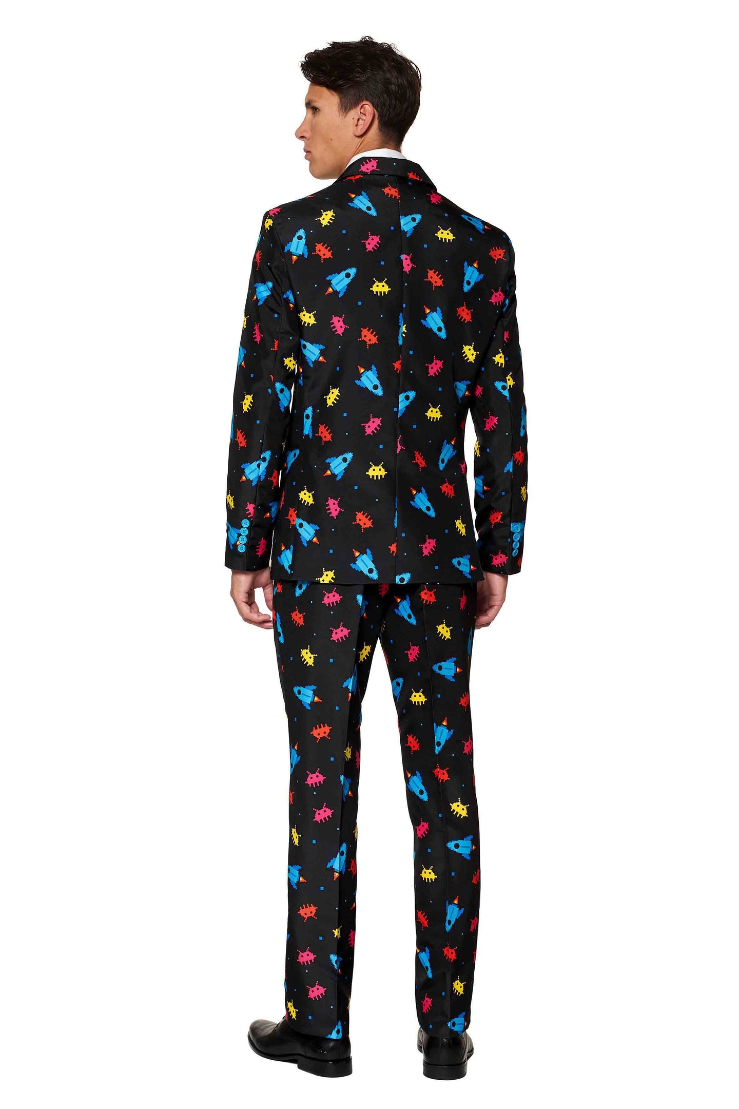 A person is wearing the Suitmeister Videogame - Game suit, which features a black base with vibrant retro video game graphics, including red, yellow, and blue space invader-like patterns. The individual is standing with their back to the viewer, highlighting the suit's design.