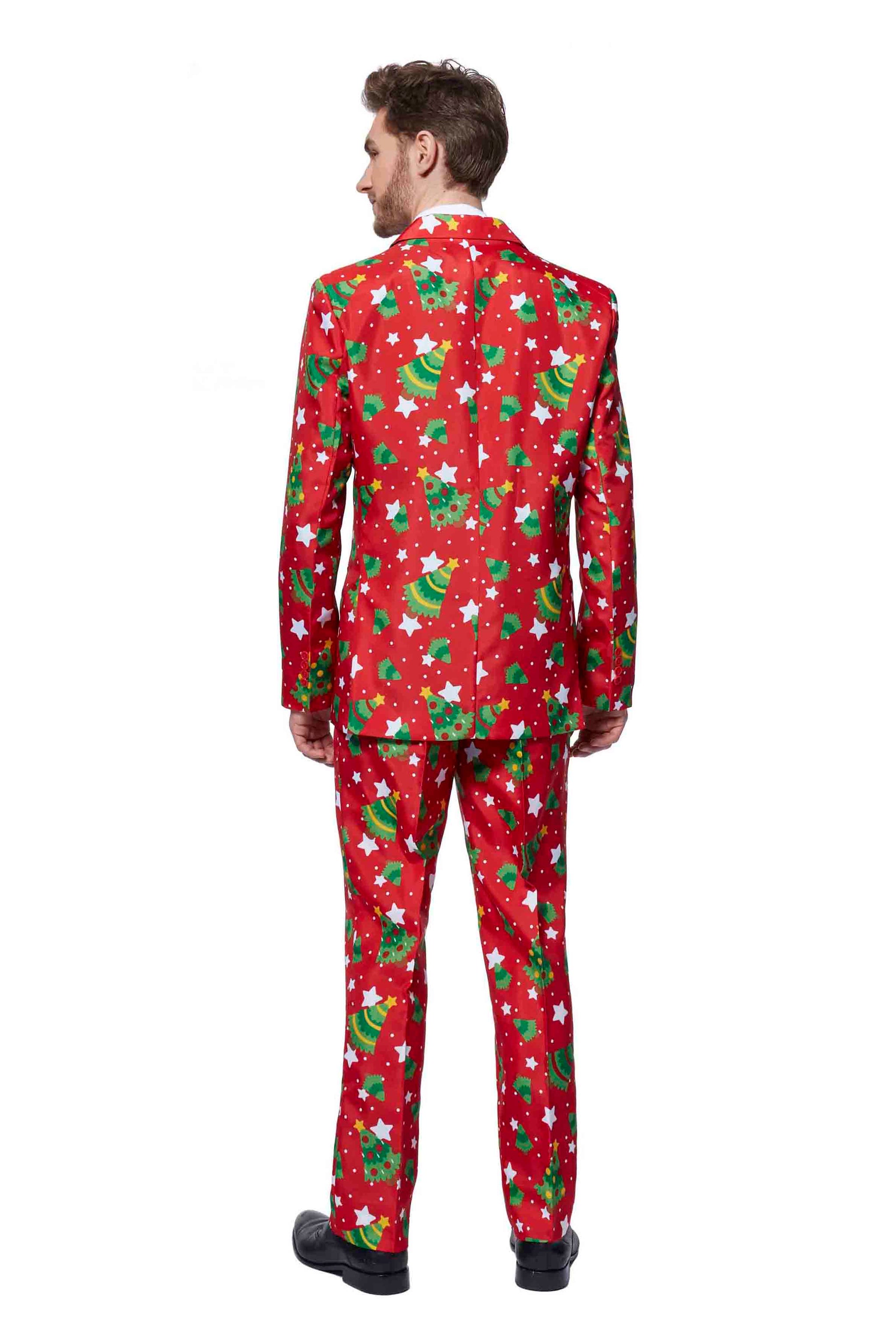 A man is dressed in a Suitmeister Christmas Trees Stars Red suit, featuring a festive design with green Christmas trees and white star patterns. He stands facing away from the camera, complemented by black shoes.